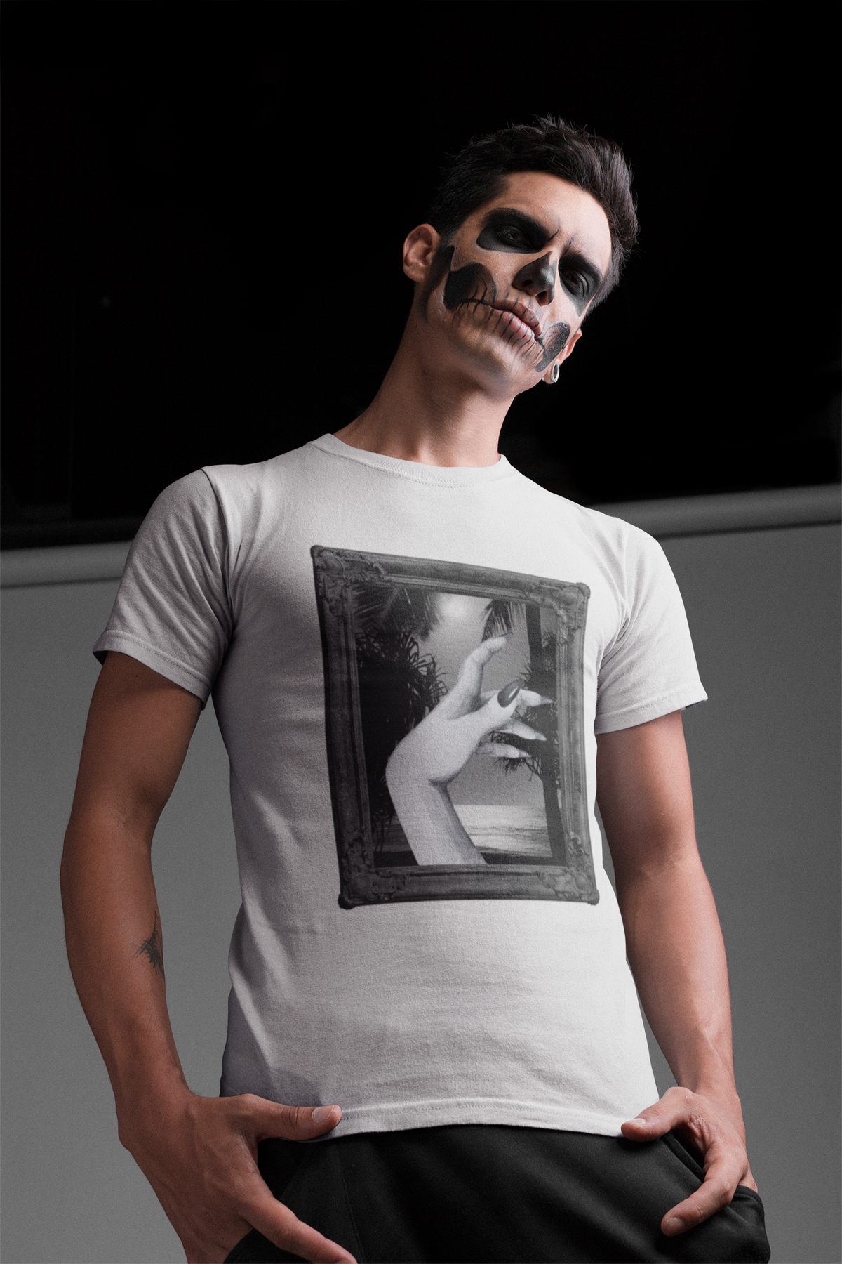 A man wearing a white crewneck t-shirt with a black-and-white graphic print of a hand reaching out of a picture frame, posed against a dark studio background.